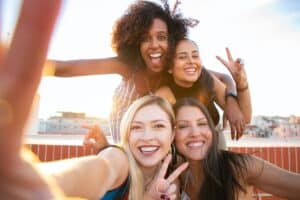 Photo by Kampus Production: https://www.pexels.com/photo/cheerful-young-diverse-women-showing-v-sign-while-taking-selfie-on-rooftop-5935235/ -- selfie