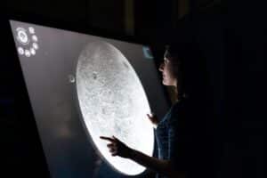 Image Title: Interactive Moon Exploration Exhibit Image Description: Visitor interacting with a touch-responsive display at an expo Alt Text: Lunar Exhibit Interaction Source: https://unsplash.com/photos/woman-in-blue-dress-holding-white-round-board-HDPbafemBI4