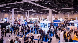 Event planners reviewing promotional strategies at a busy trade show conference with attendees networking in the background